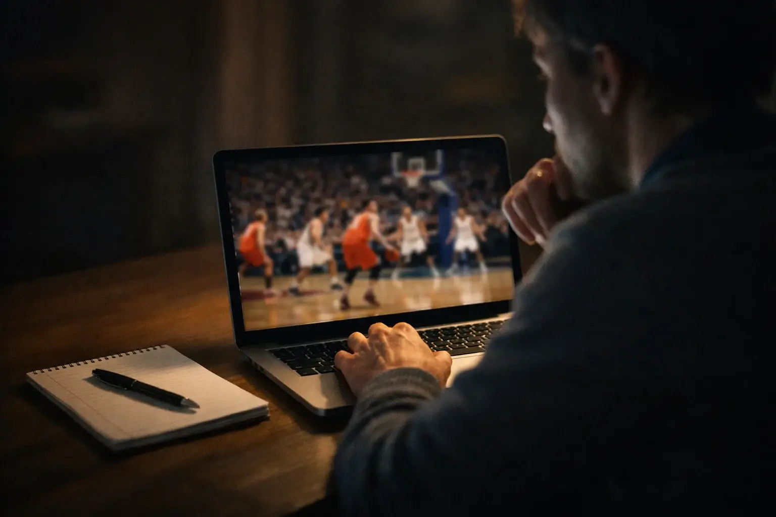 Persoon die NBA quoteringen vergelijkt op een laptop met basketbalwedstrijd op de achtergrond